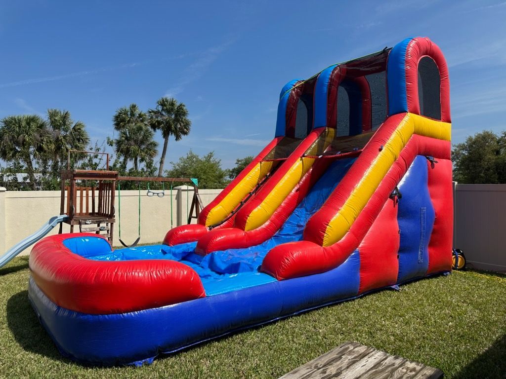A vibrant red, blue, and yellow inflatable water slide sits on a residential lawn on a sunny day.