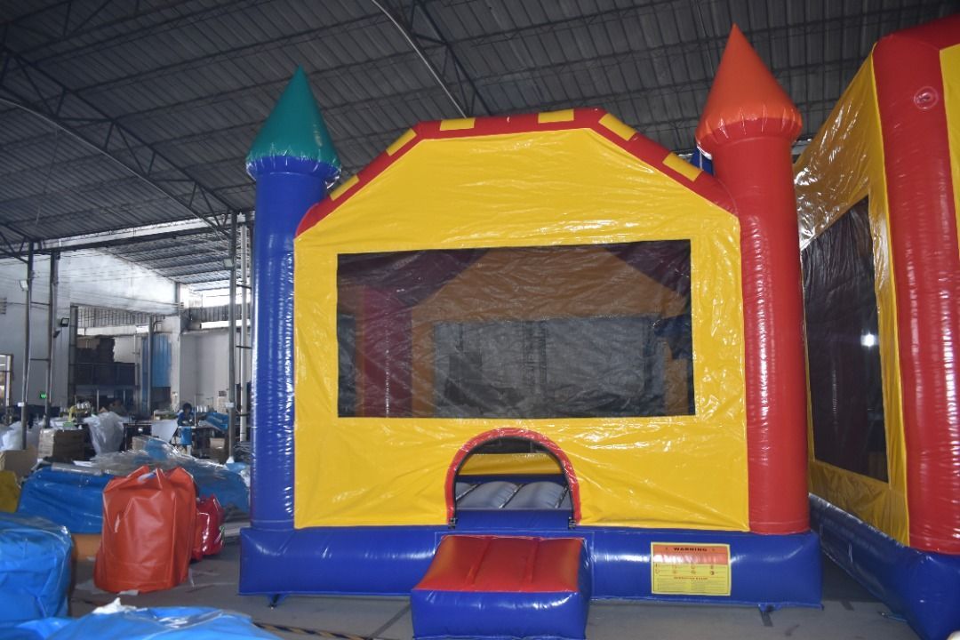 A colorful inflatable bounce house with a yellow front, red and blue accents, and turrets, sitting in a warehouse.