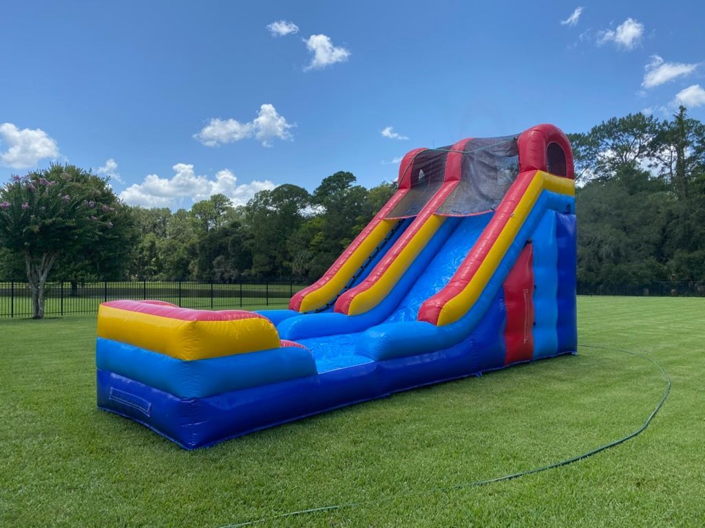 A colorful inflatable water slide with blue, yellow, and red sections standing in a grassy field under a sunny sky.
