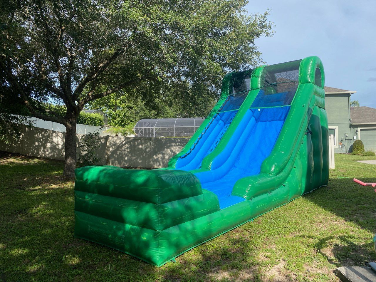 A large, inflatable green and blue water slide sits on a residential lawn.