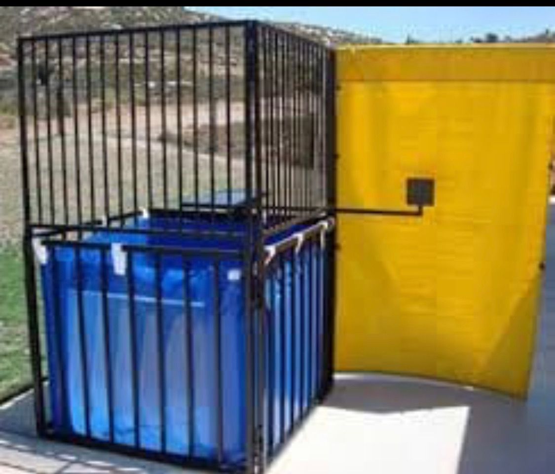 A classic carnival dunk tank with a blue water basin, black metal cage, and a yellow backdrop target.
