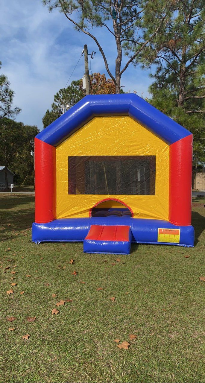 A colorful red, yellow, and blue inflatable bounce house sits on a grassy lawn outdoors.