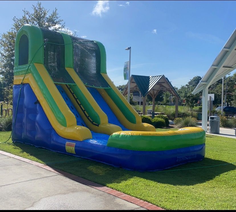 A blue, green, and yellow inflatable slide set up on a grassy lawn under a clear blue sky.