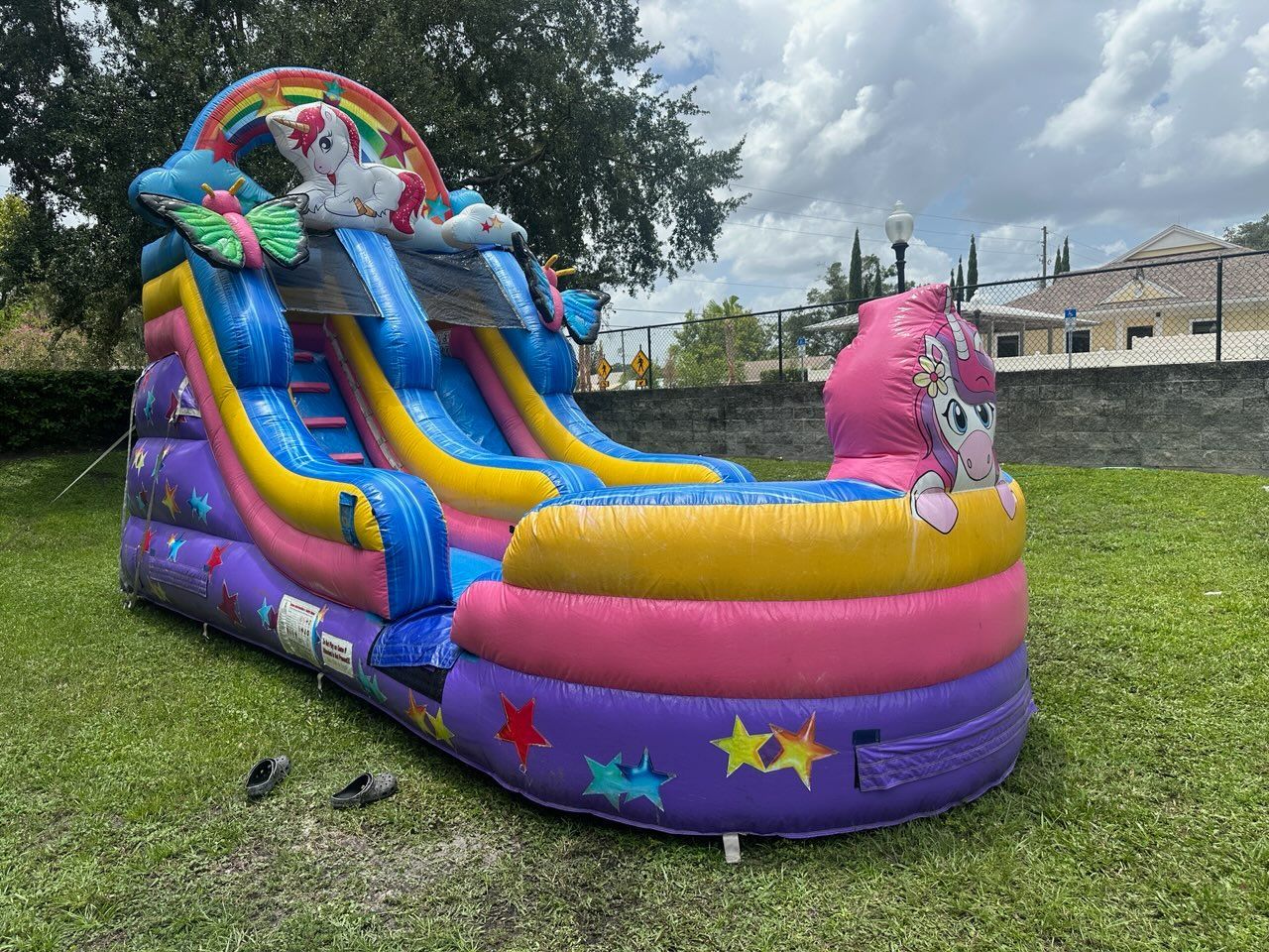 A colorful, inflatable unicorn-themed water slide sitting on a grassy lawn in front of a stone wall.