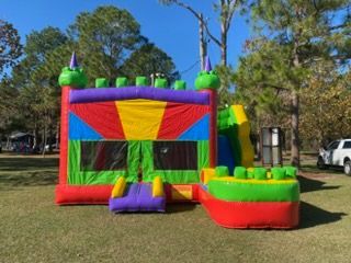 A colorful inflatable bounce house with a slide and a small ball pit area set up on a grassy lawn outdoors.