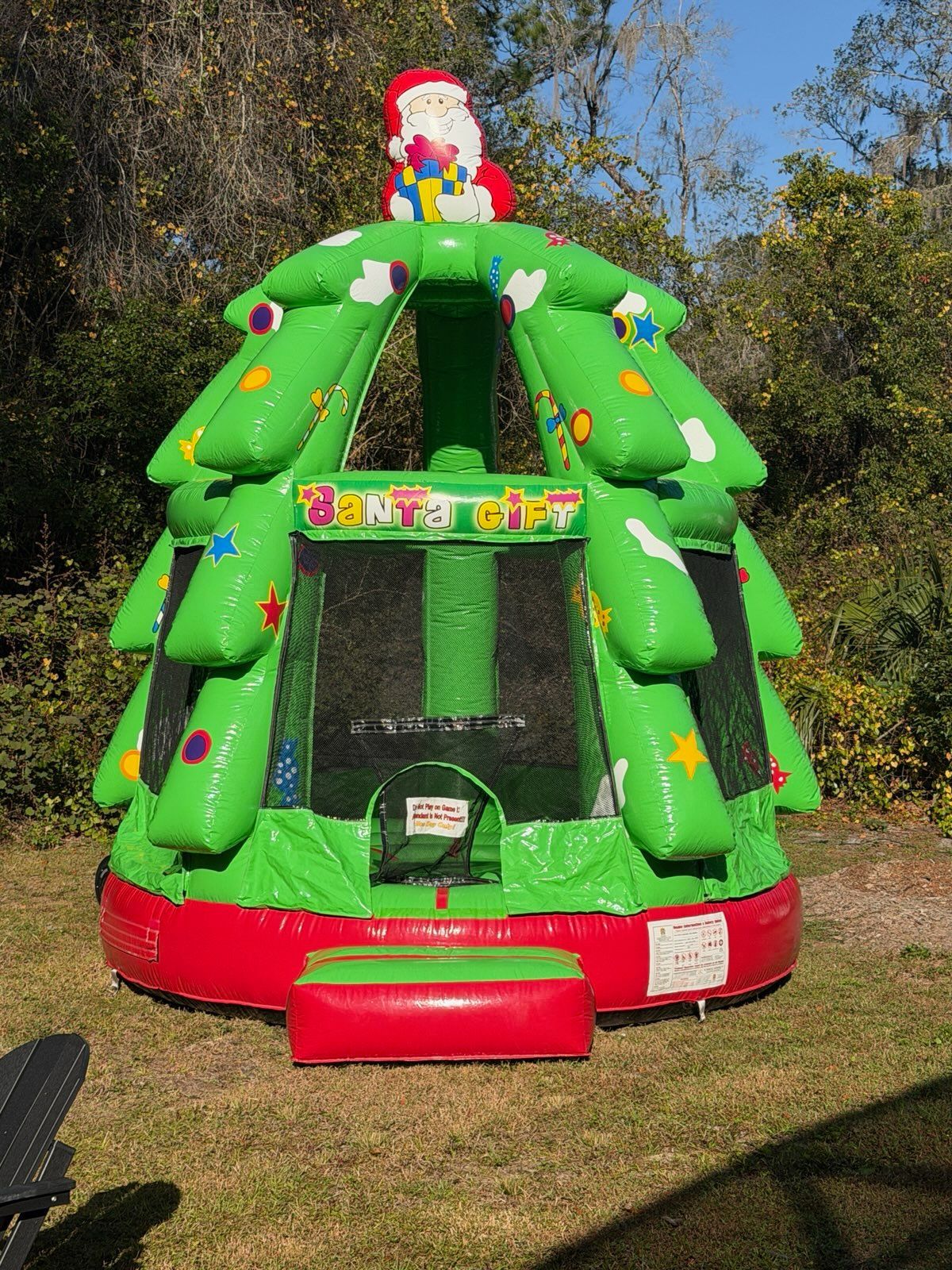 A green, inflatable bouncy house shaped like a Christmas tree topped with Santa, set outdoors on grass.