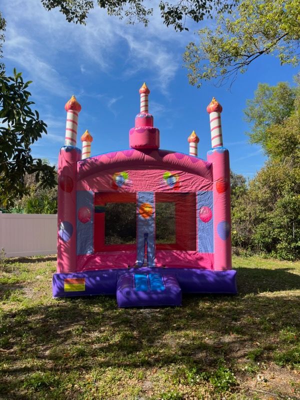 A pink inflatable castle bounce house with candle-shaped pillars, situated on a grassy lawn outdoors.