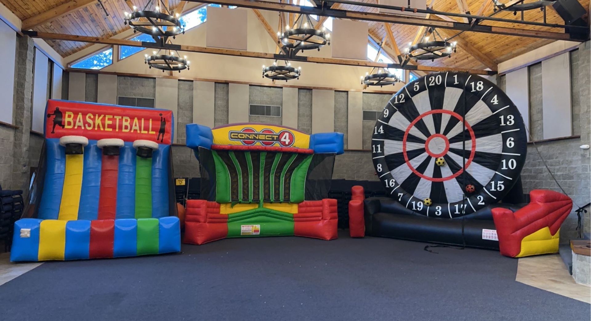 Three large inflatable games, including a basketball hoop, a four-in-a-row grid, and a giant dartboard, stand in a room.