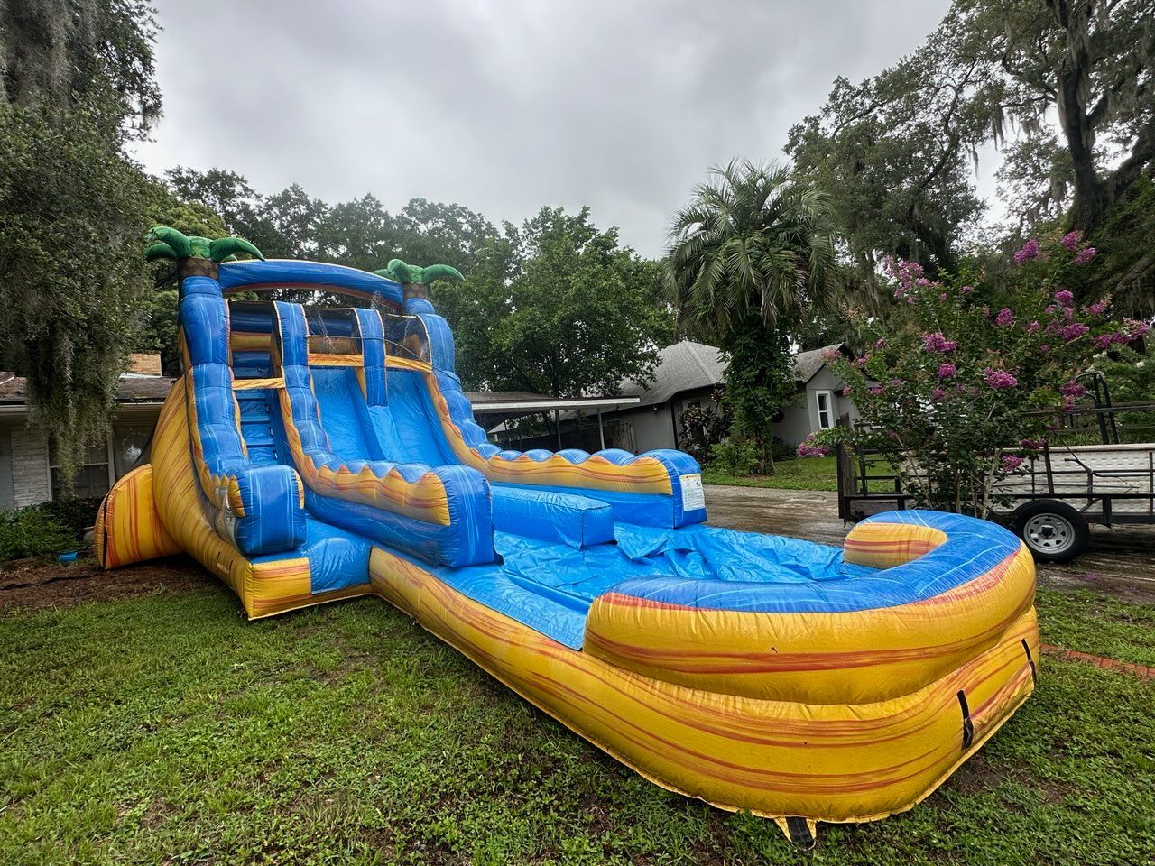 A large, inflatable blue and yellow tropical-themed water slide set up on a grassy lawn in front of a house.