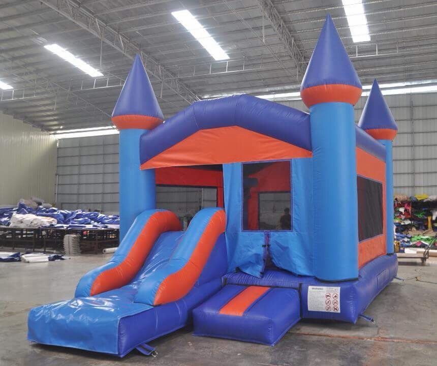 A blue and orange inflatable bouncy castle with a slide, standing in a large indoor warehouse.