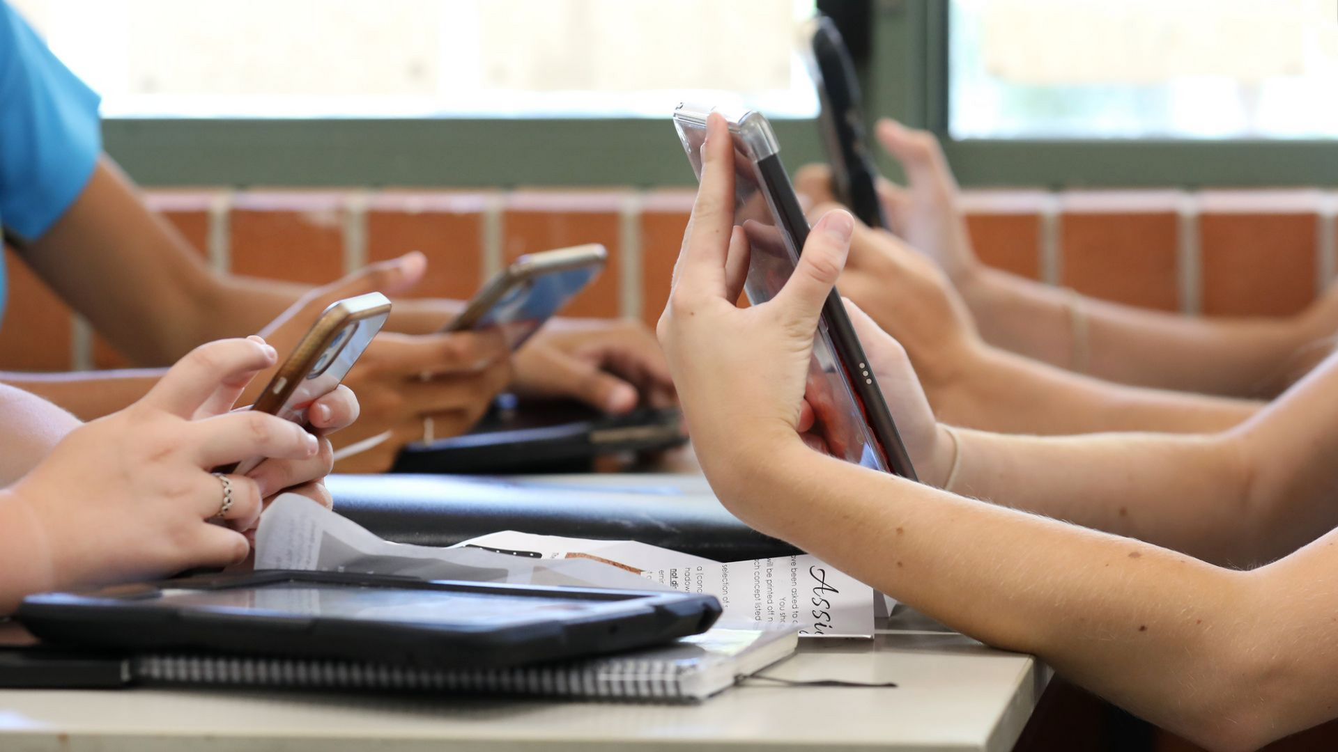 Hands holding smartphones, several people at a table, some devices resting on the table. Hands holding smartphones, several people at a table, some devices resting on the table.