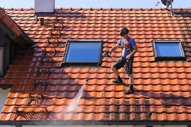 A man is cleaning the roof of a house with a high pressure washer.