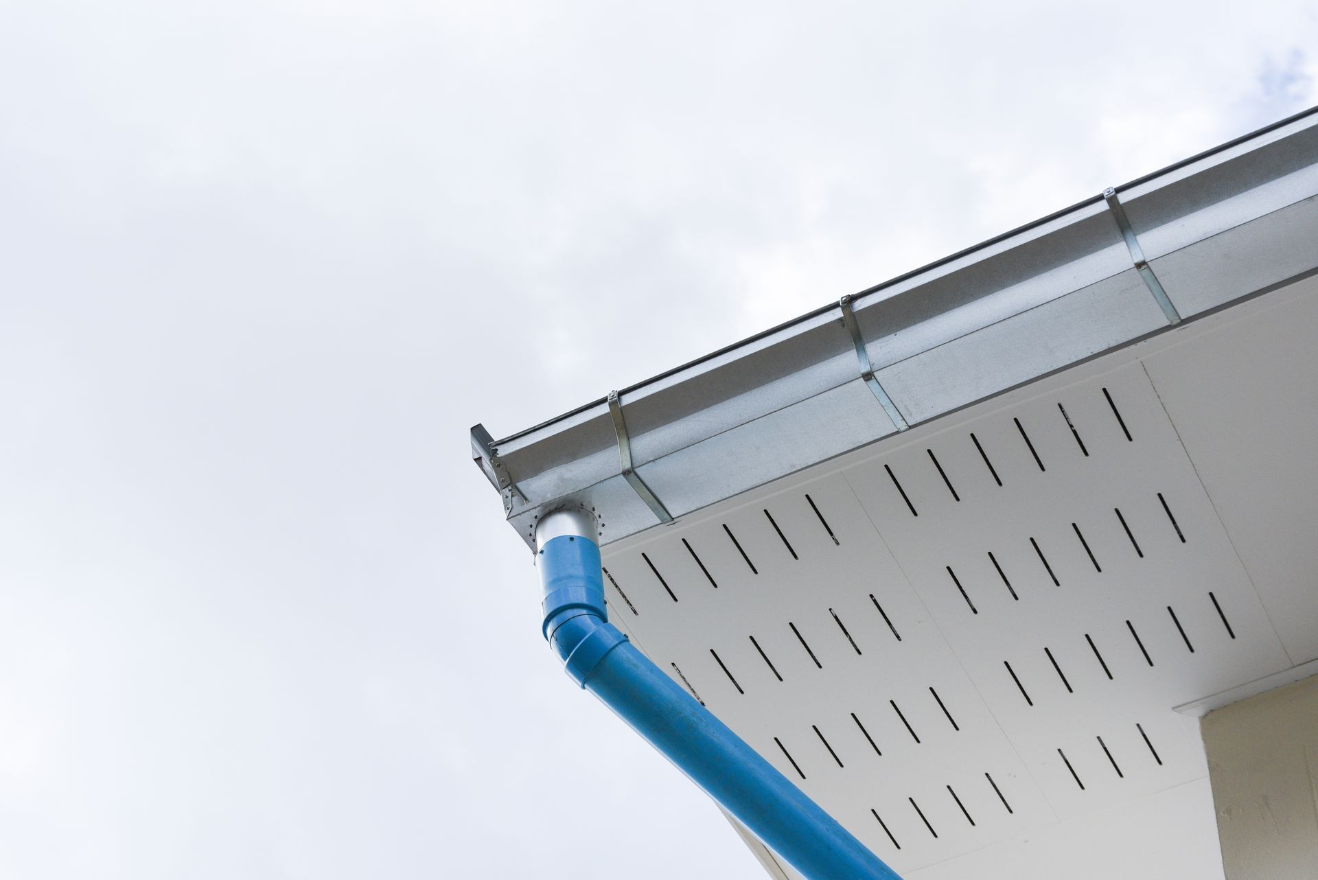 A man is fixing a gutter on a house with a drill.