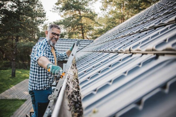 A man is cleaning a gutter on the roof of a house.