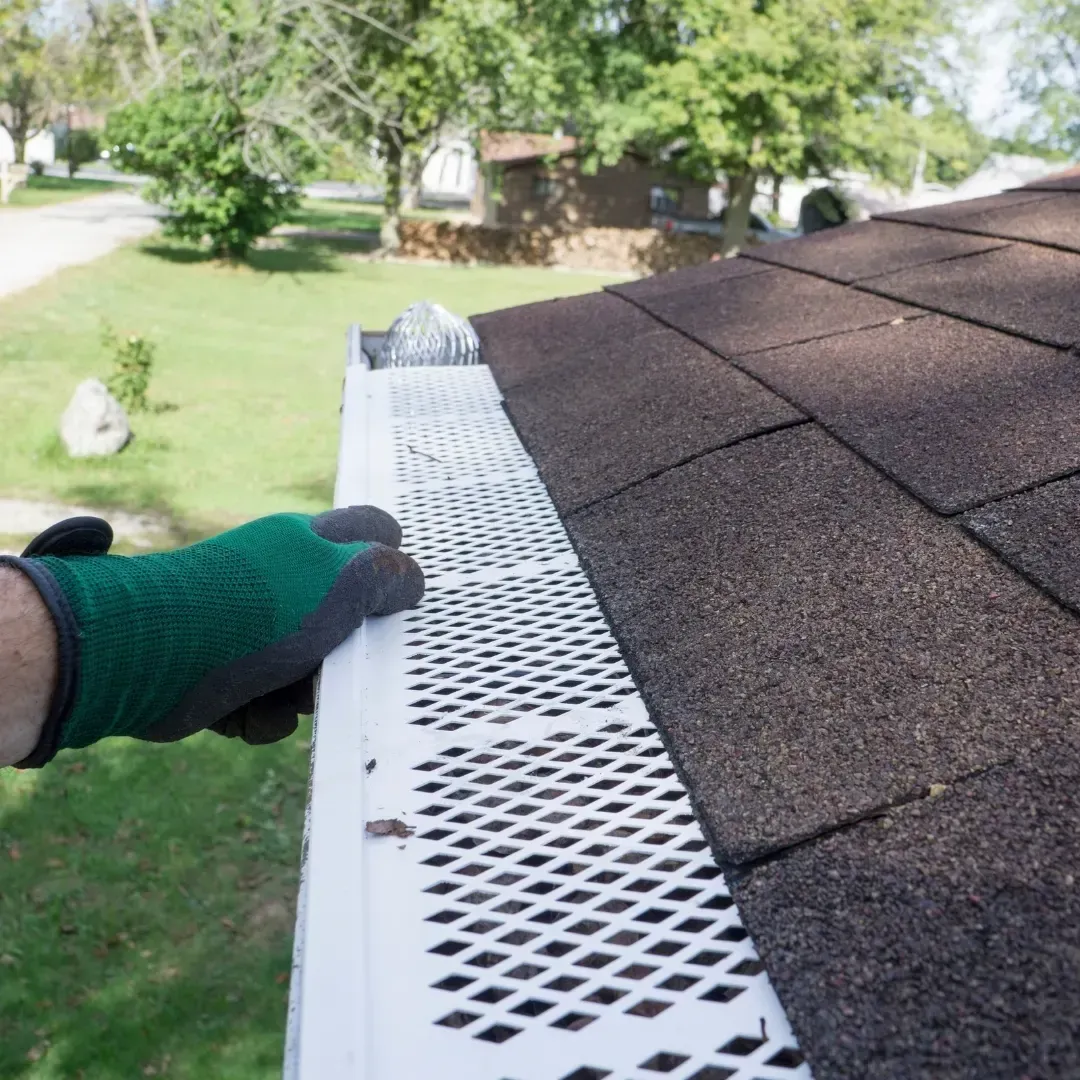 Gloved hand placing white gutter guard along a shingled roof edge outside Gloved hand placing white gutter guard along a shingled roof edge outside