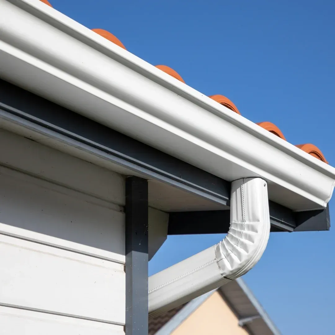 White gutter and downspout on house roof against blue sky White gutter and downspout on house roof against blue sky