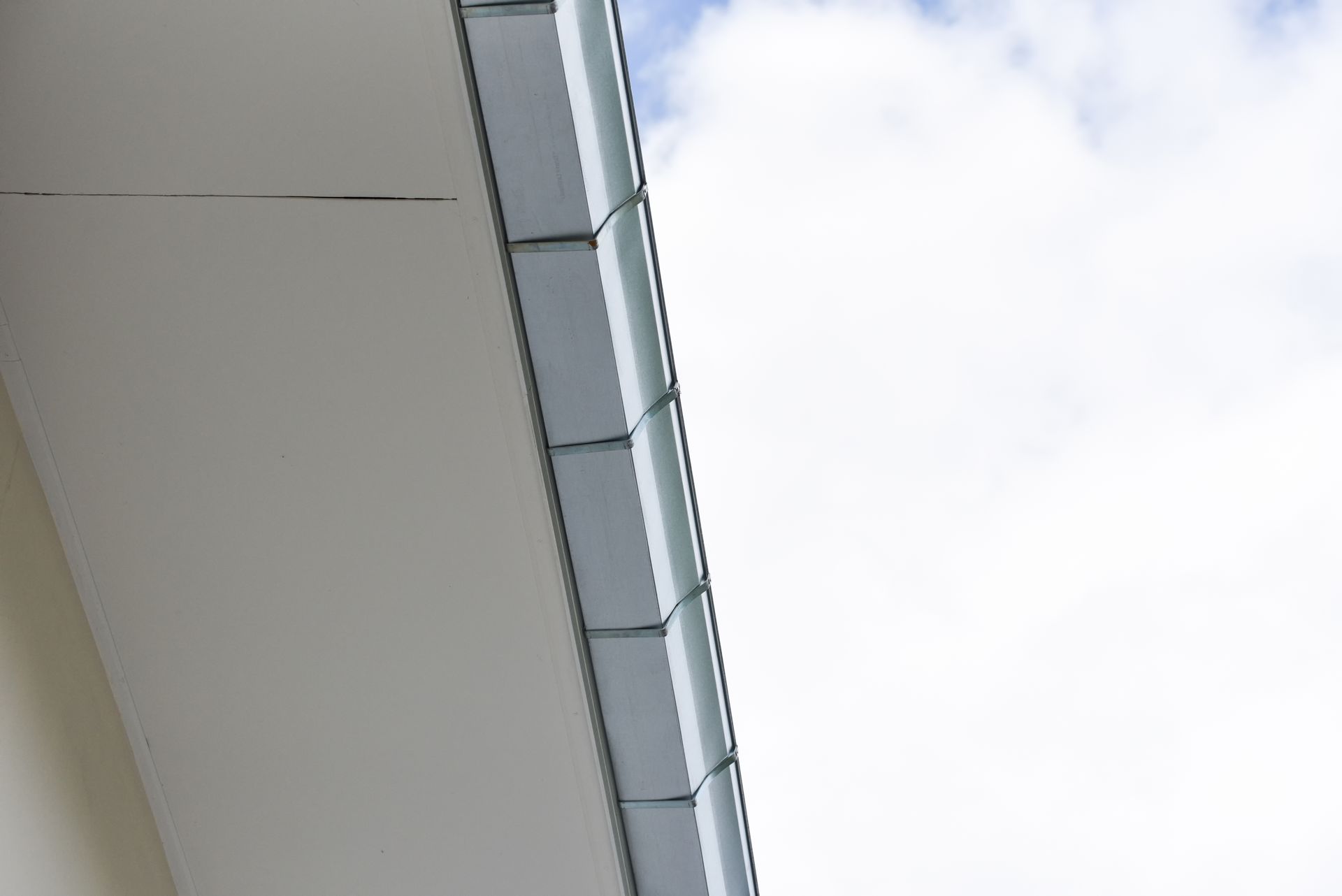 A close up of a gutter on the side of a building with a cloudy sky in the background.