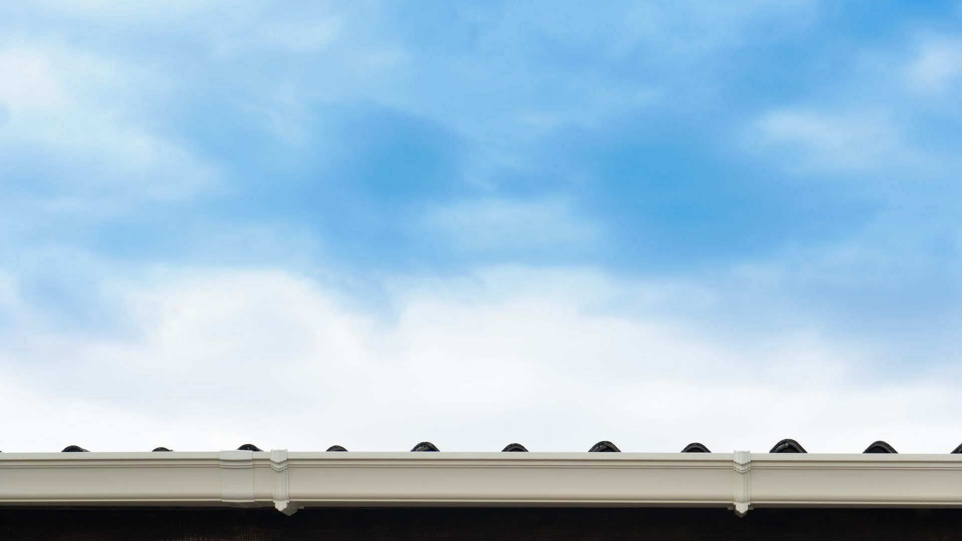 A close up of a gutter on a roof with a blue sky in the background.