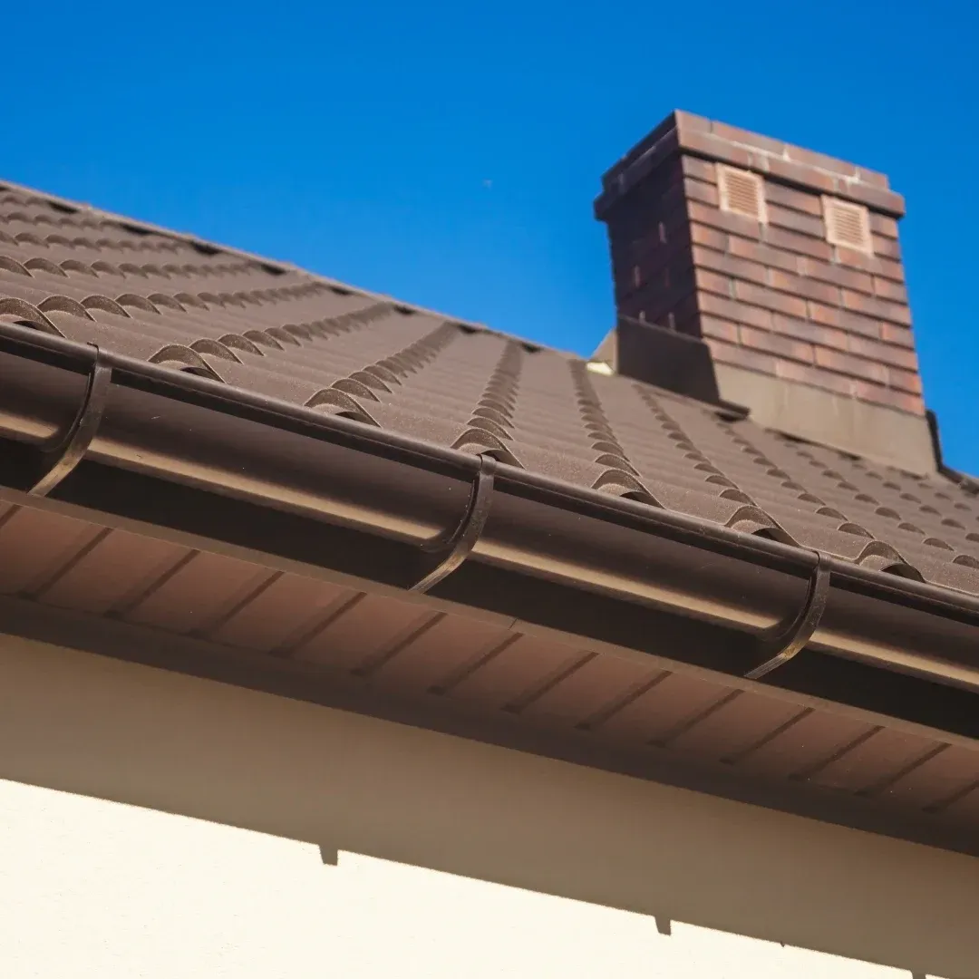 Brown shingled roof with a brick chimney against a clear blue sky