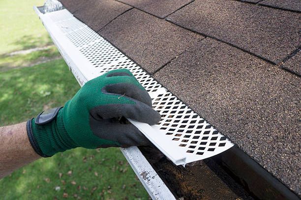 A person wearing gloves is cleaning a gutter on a roof.