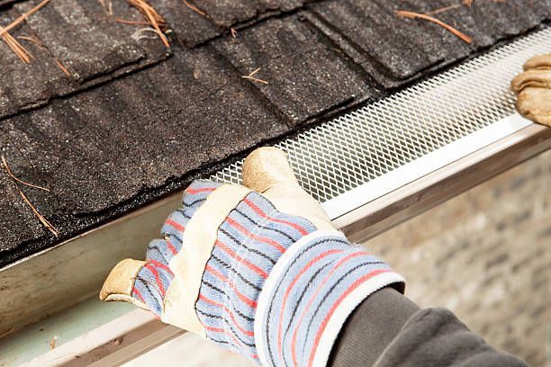 A person wearing gloves is cleaning a gutter on a roof.