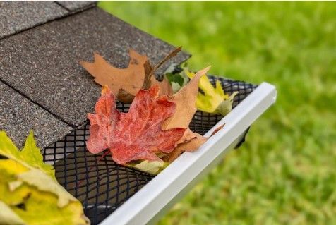 A gutter with leaves coming out of it and a roof in the background.