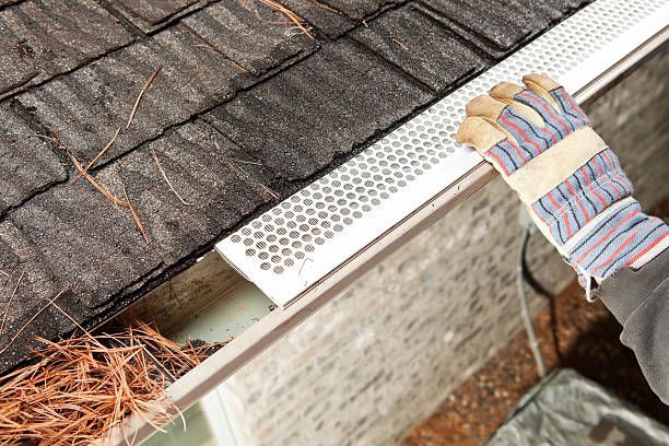 A person wearing gloves is cleaning a gutter on a roof.