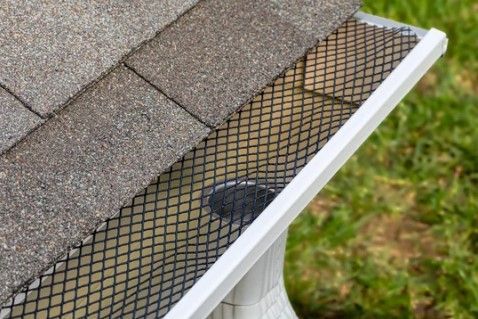 A gutter with leaves coming out of it and a roof in the background.