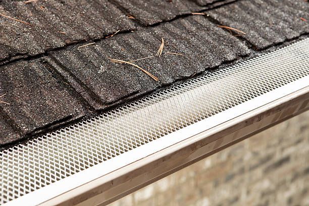 A close up of a gutter on a roof with shingles.