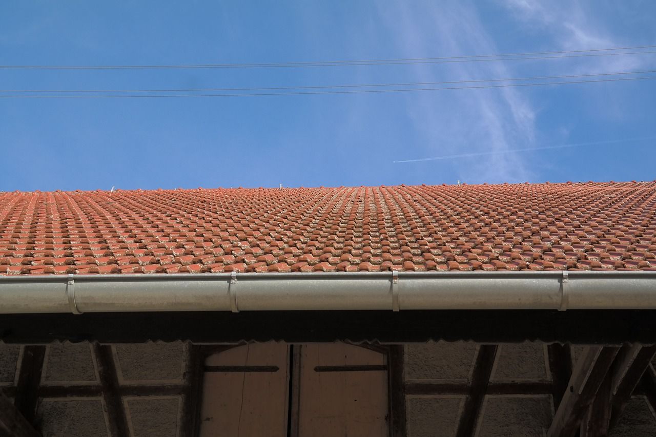 A red tiled roof with a white gutter and a blue sky in the background.