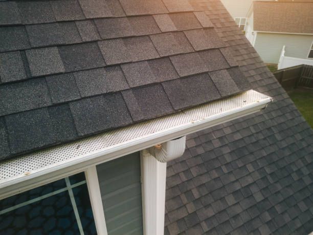 A close up of a roof with shingles and a gutter on a house.