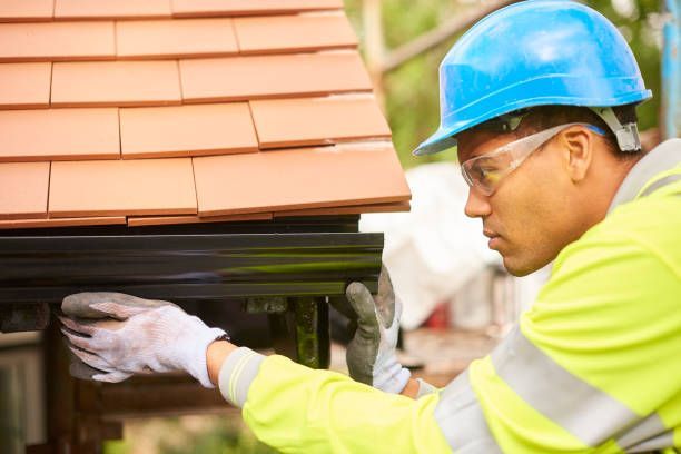 A man wearing a hard hat and safety glasses is working on a gutter on a roof.