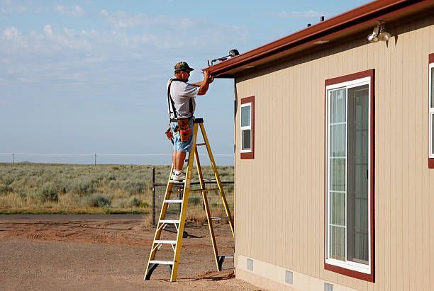 A man is standing on a ladder working on the roof of a house.