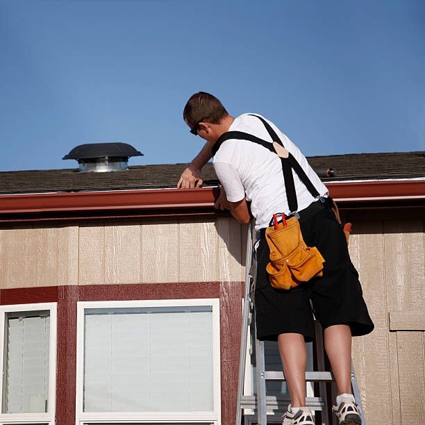 A man is standing on a ladder working on the roof of a house