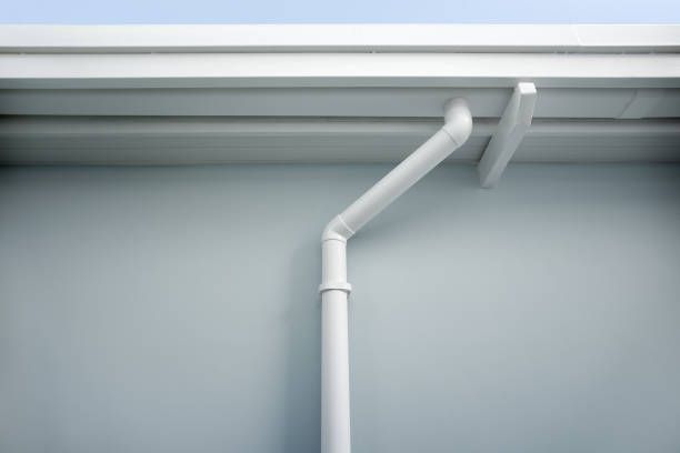 A white gutter on the side of a building with a blue sky in the background.