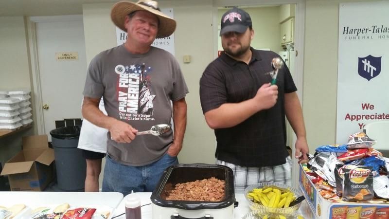 Two men are standing in front of a table with food and a sign that says we appreciate you