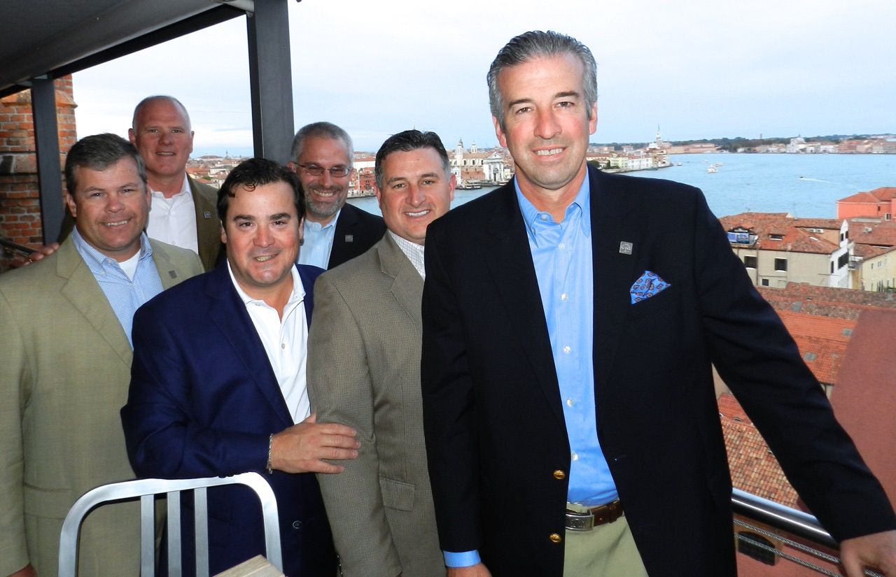 A group of men are posing for a picture on a balcony overlooking a body of water.
