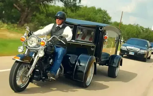 A man is riding a motorcycle with a trailer attached to it.