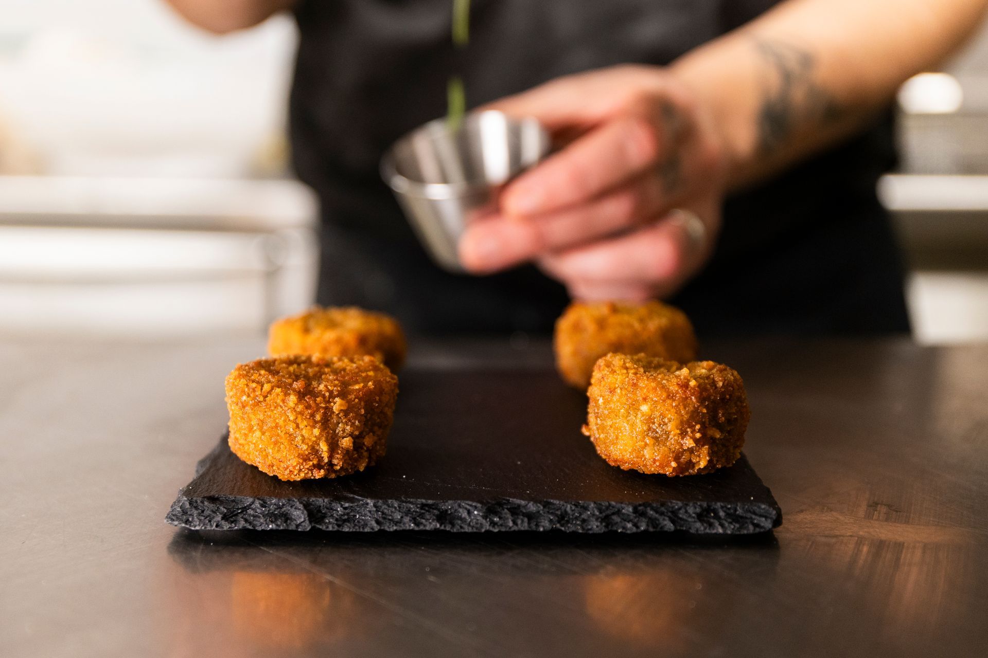 Una persona sta preparando del cibo fritto su un piatto nero.