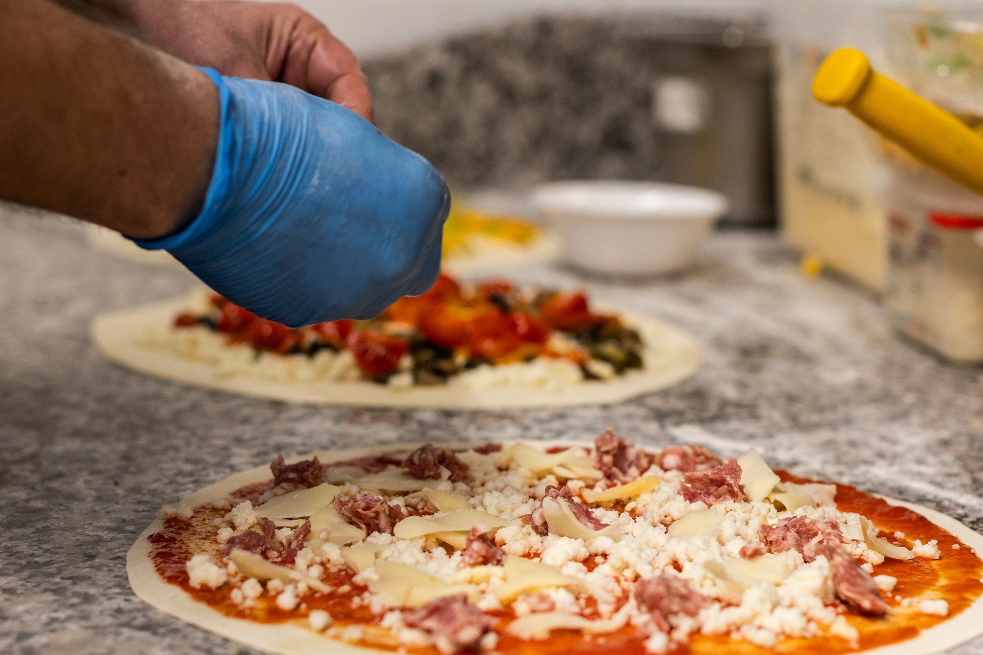 Una persona che indossa guanti blu sta spalmando il formaggio su una pizza.