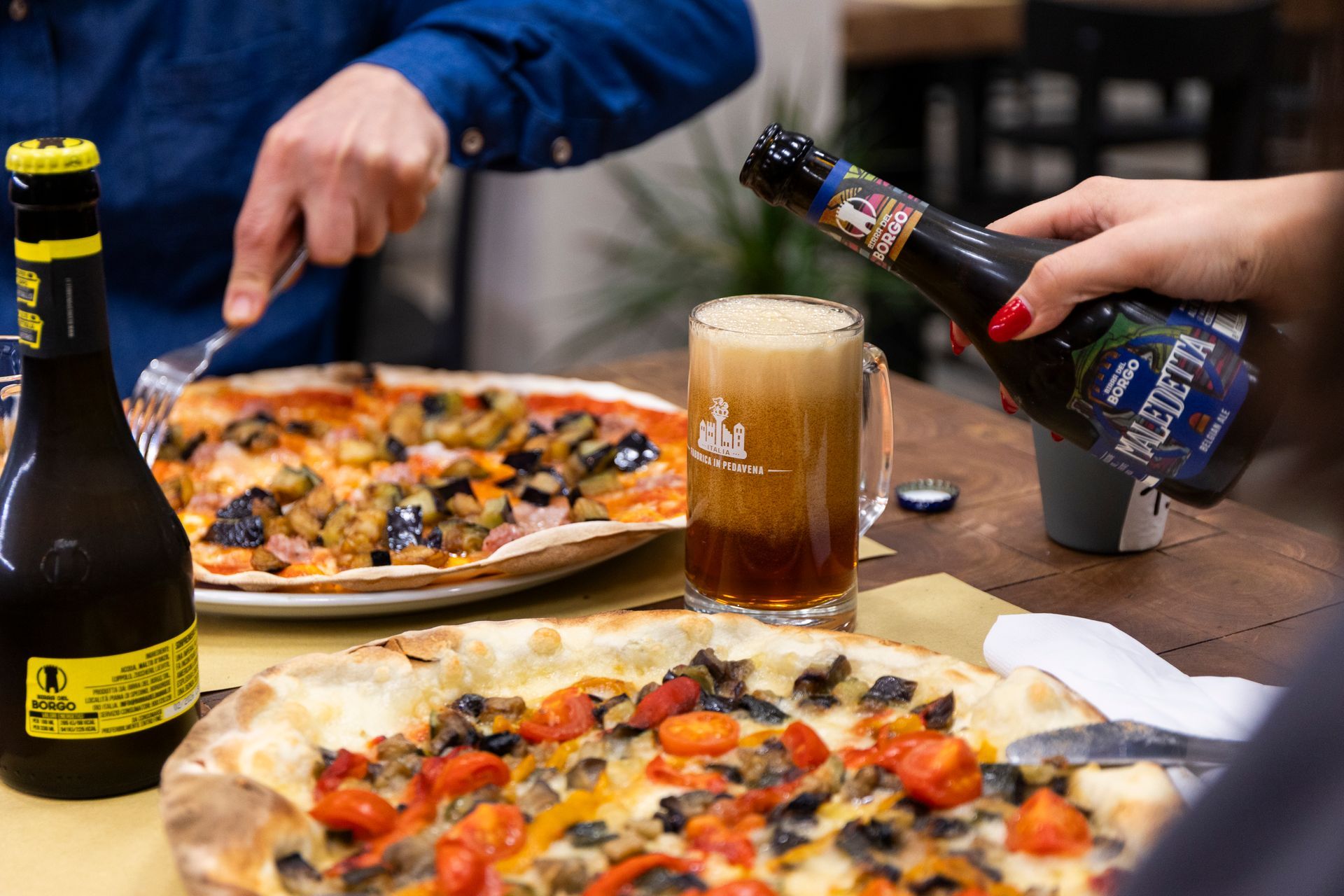 Una persona versa della birra in un bicchiere accanto a una pizza su un tavolo.