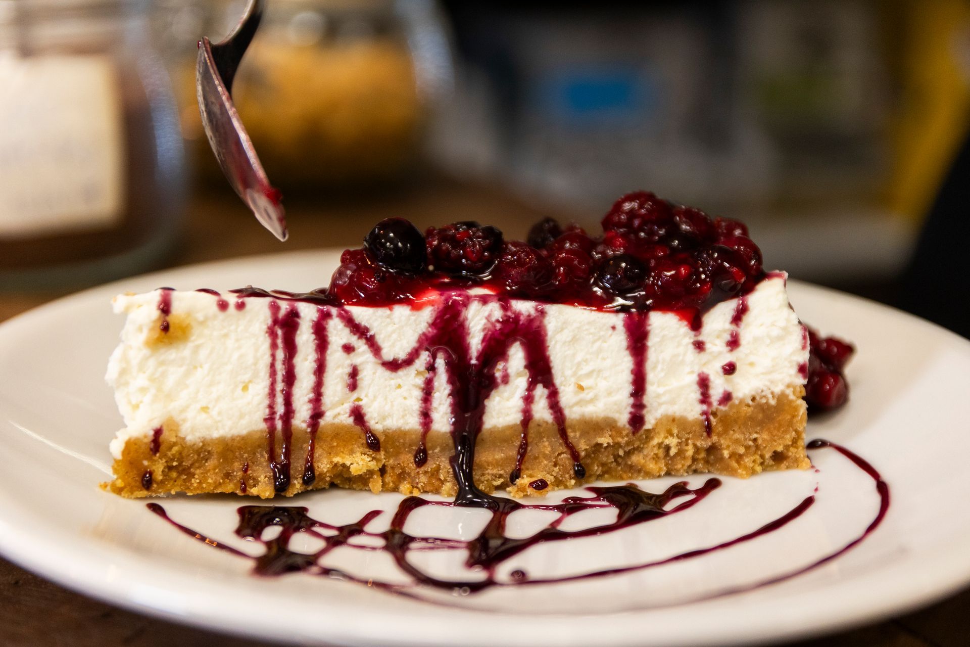 Una fetta di cheesecake con frutti di bosco e salsa al cioccolato su un piatto bianco.
