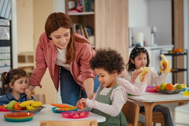 Teacher and children at a table preparing and eating fruits and vegetables.