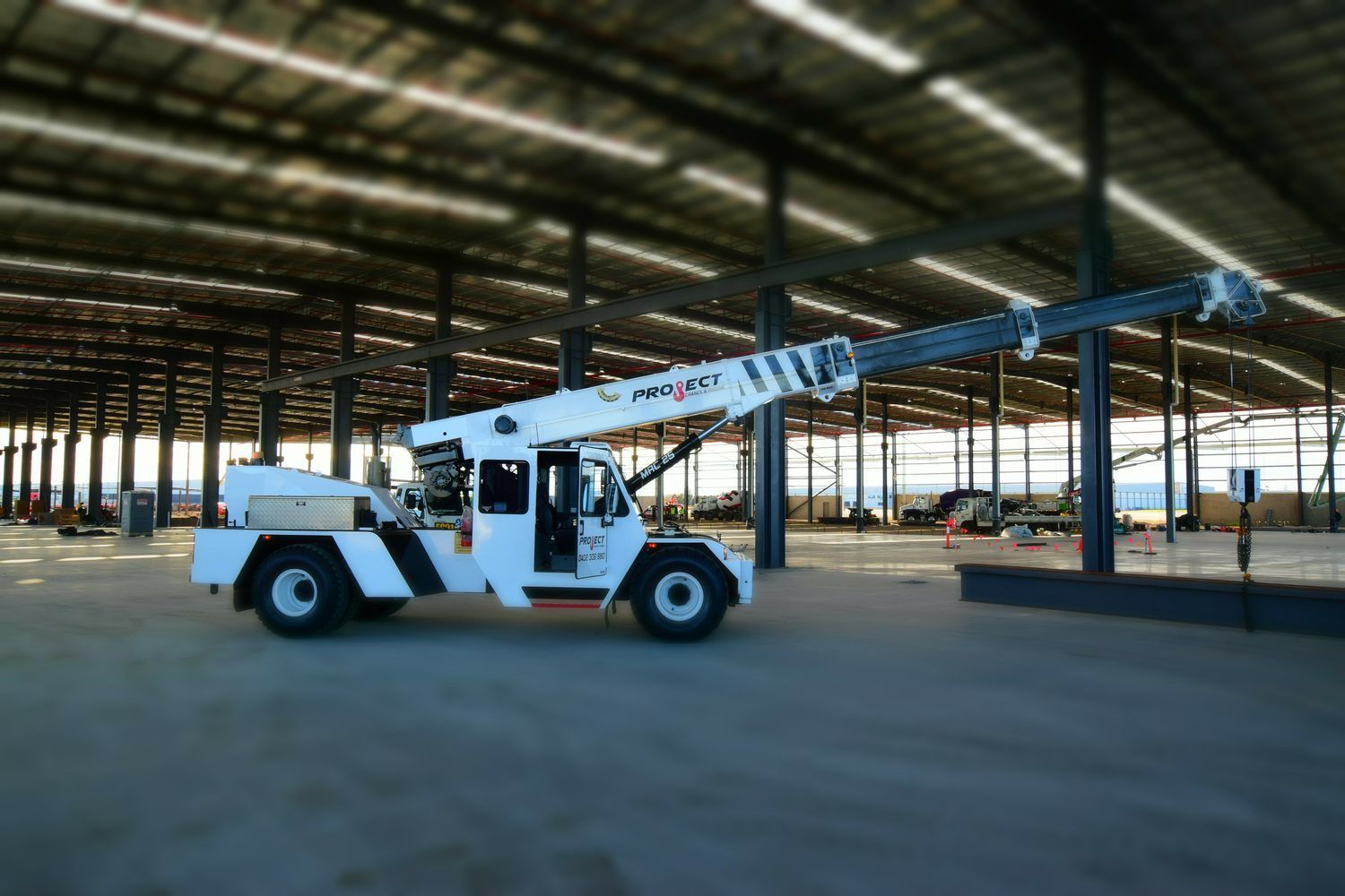 A white truck with a long crane is driving through a large warehouse.