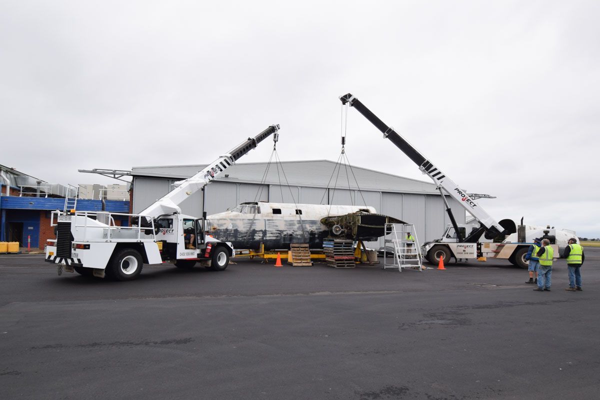 A crane is lifting a plane into a hangar.