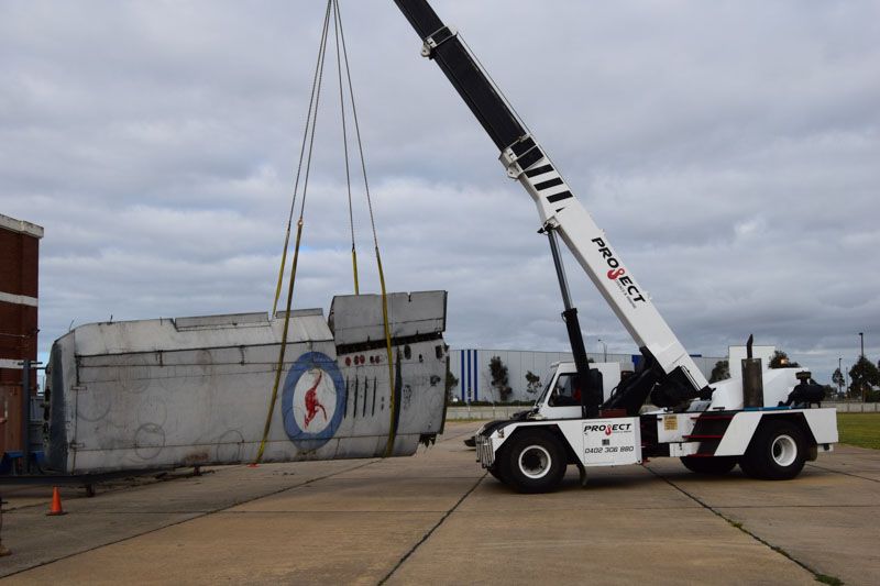 A crane is lifting a large piece of concrete in a parking lot.