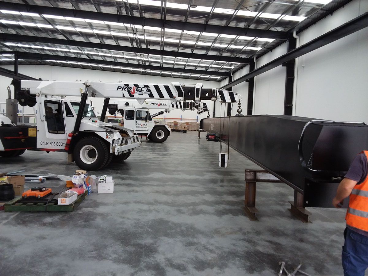 A man in an orange vest is working on a crane in a warehouse