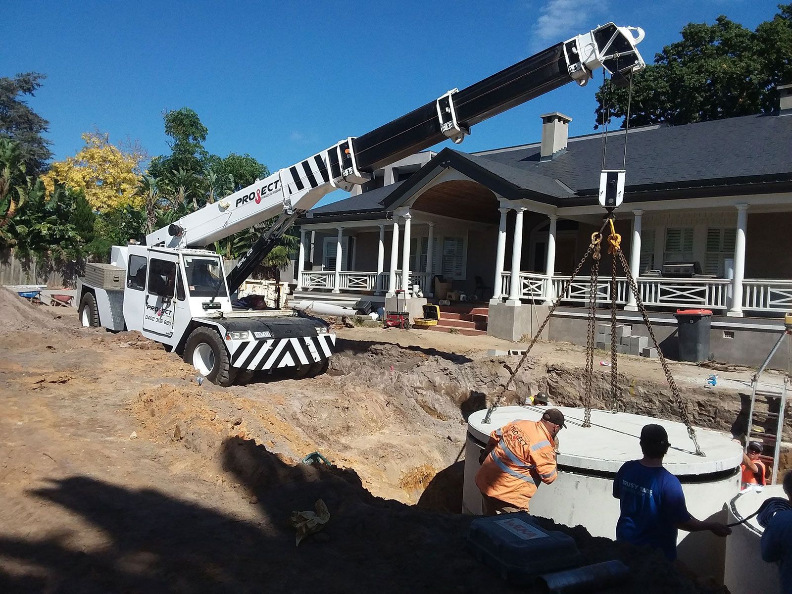 A large crane is being used to lift a concrete block in front of a house