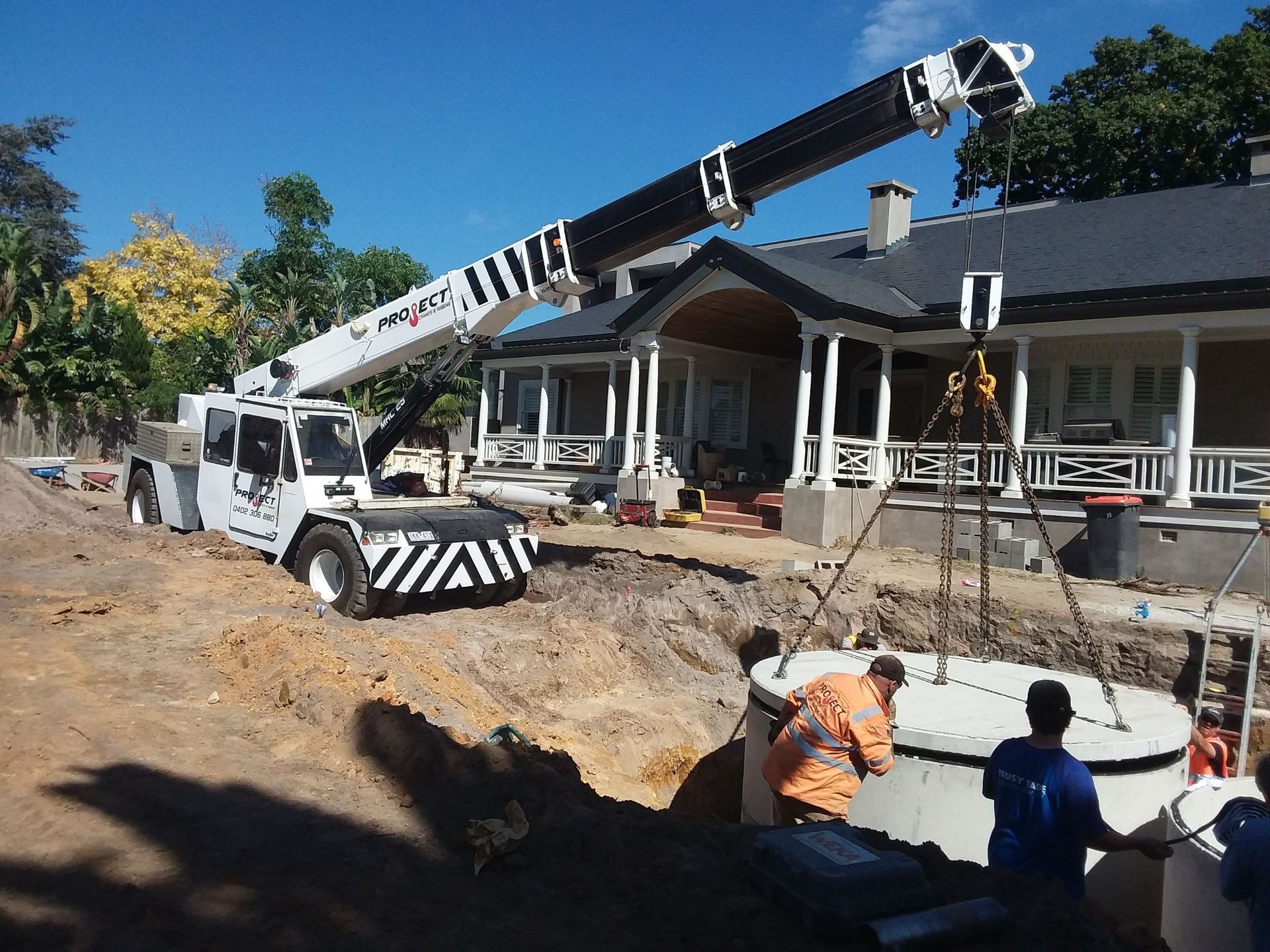 A crane is lifting a large white object in front of a house