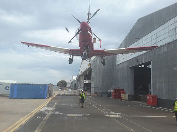 A red airplane is being lifted into the air by a crane